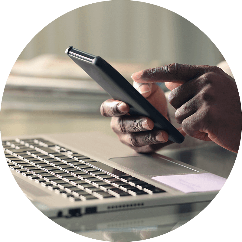 Hand holding a mobile phone in front of a computer.