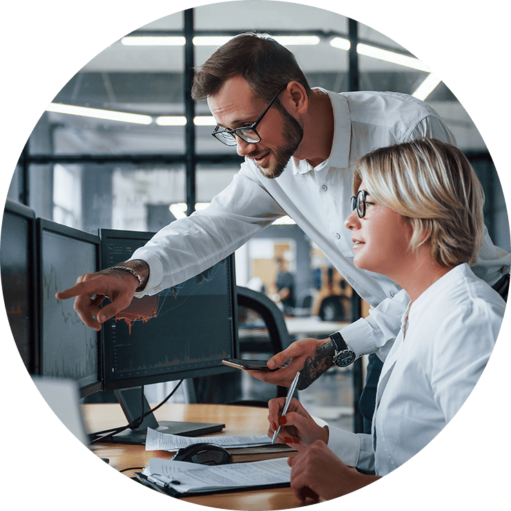Two professionals analyzing data on computer screens in a modern office, collaborating on insights or solutions.