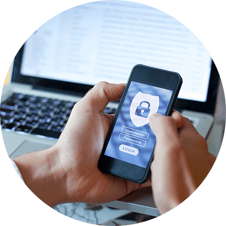 A person logging into a secure app on a smartphone, with a laptop in the background.