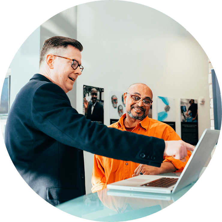 Two men talking and smiling in front of a computer screen.