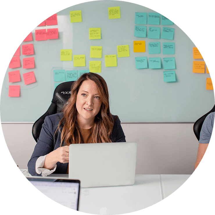A lady sitting in front of a laptop in a room with sticky notes on the background.